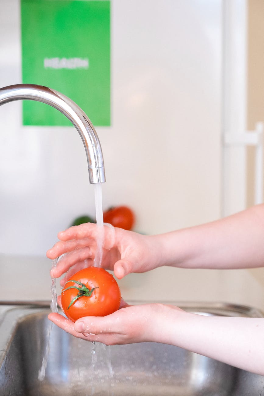 person washing a tomato fruit with water