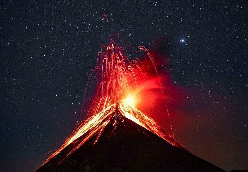 volcano erupting at night under starry sky